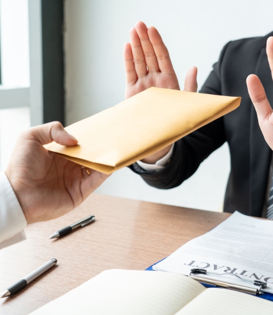 Obrázok znázorňuje odmietnutie obálky s dokumentmi alebo peniazmi v kancelárskom prostredí, čo môže symbolizovať etiku, transparentnosť alebo odmietnutie úplatku.