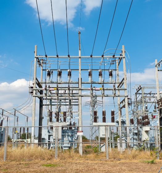 Elektrická rozvodňa s transformátormi a vodičmi pod modrou oblohou – distribúcia a prenos elektrickej energie.